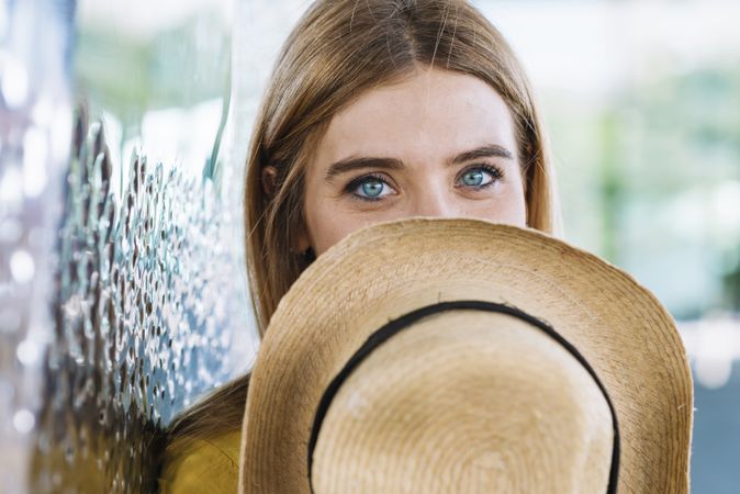 Woman with blue eyes covering face with straw hat