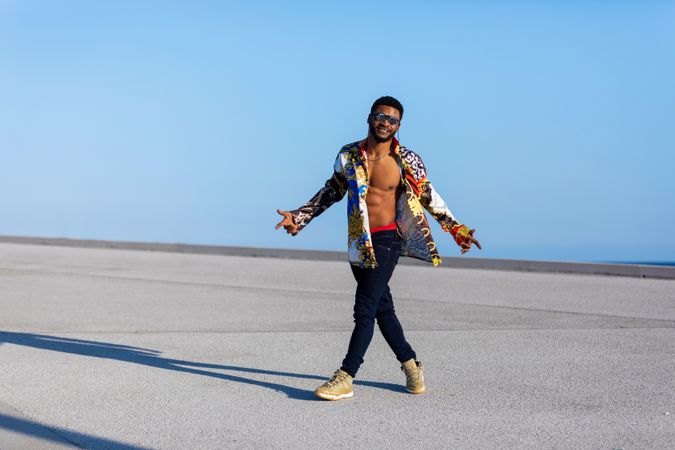 Black man walking while wearing eyeglasses with open shirt against blue sky on sunny day