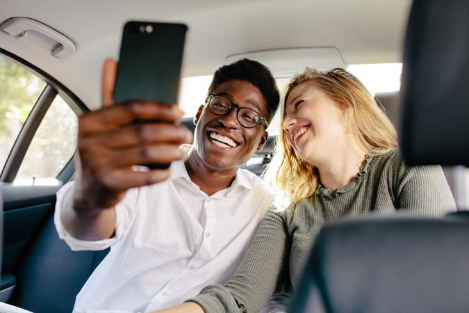 Smiling man with girlfriend taking selfie while traveling in a car