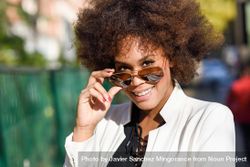 Smiling stylish female looking up from aviators sunglasses on street 4OQPL0