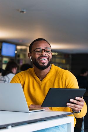 Cheerful man with earbuds using tablet and laptop at table