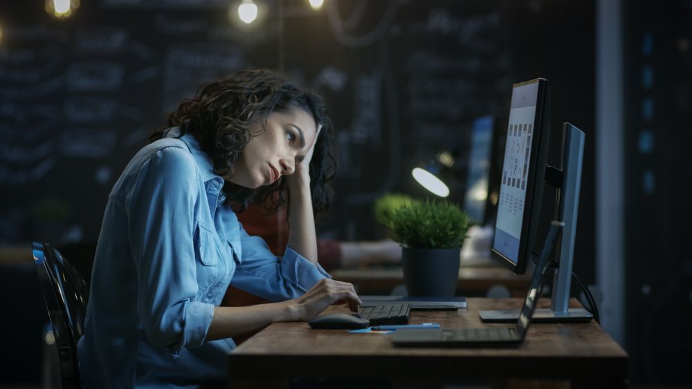 Tired, Overworked Female Financier Holds Her Head in Hands while Working on a Personal Computer