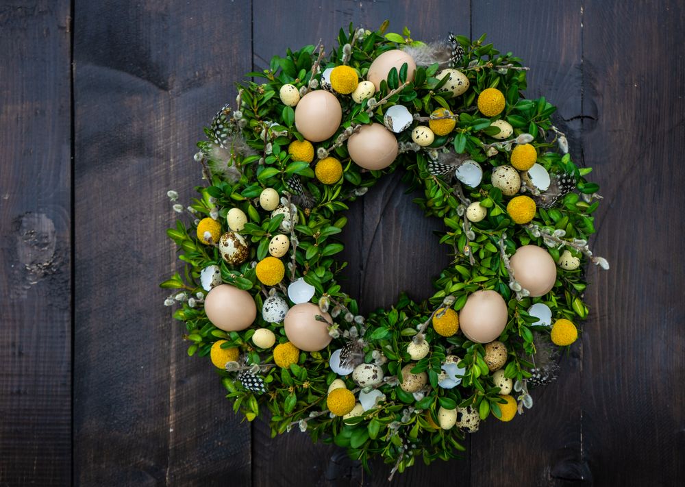 Easter card concept with fresh wreath with decorative eggs and feathers hanging on door