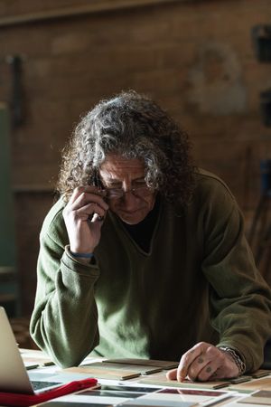 Man talking on smartphone and typing on laptop in workshop