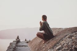 Woman meditating on castle wall overlooking sea