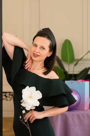 Woman posing with white flower, smiling at birthday party.