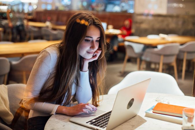 Brunette woman in a restaurant reading her e-mails on her laptop