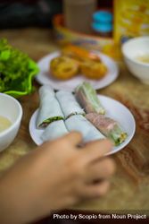 Cropped image of a hand beside vegetable rice rolls on plate on wooden table 4M7lk0