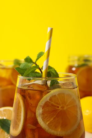 Cold tea with orange slices and mint leaves on a yellow background