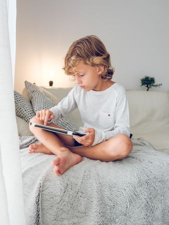 Focused boy sitting on soft plaid and browsing tablet