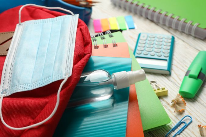 School supplies with medical mask and sanitizer on wooden background, close up