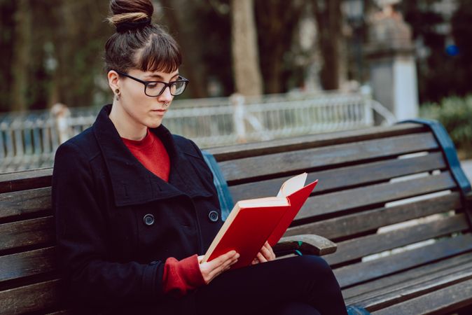 Young woman reading book on bench in park