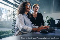 Smiling woman wearing headset working on computer with manager standing by 433d14