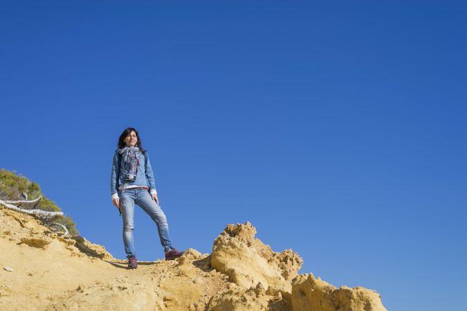 Confident female dressed in blue standing atop coastal rocks