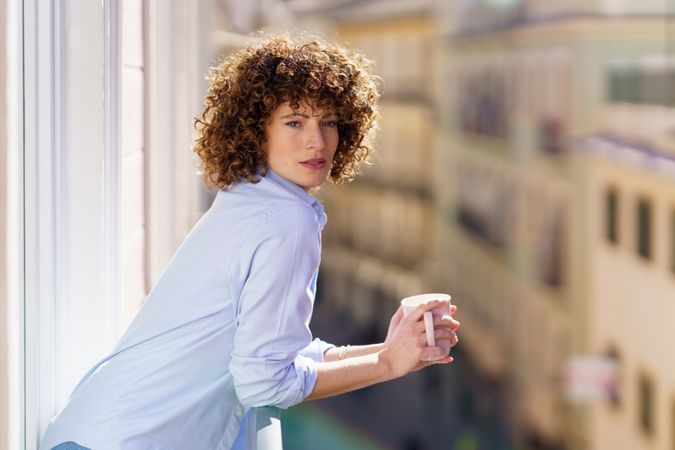 Woman with mug of coffee leaning on balcony