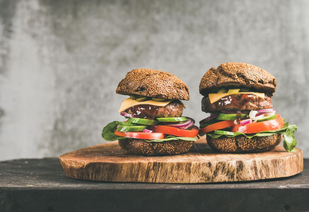 Two cheeseburgers, stacked with fresh vegetables, on wooden board, with copy space