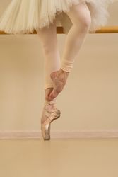 Ballet dancer practicing at barre, one foot in pointe shoes