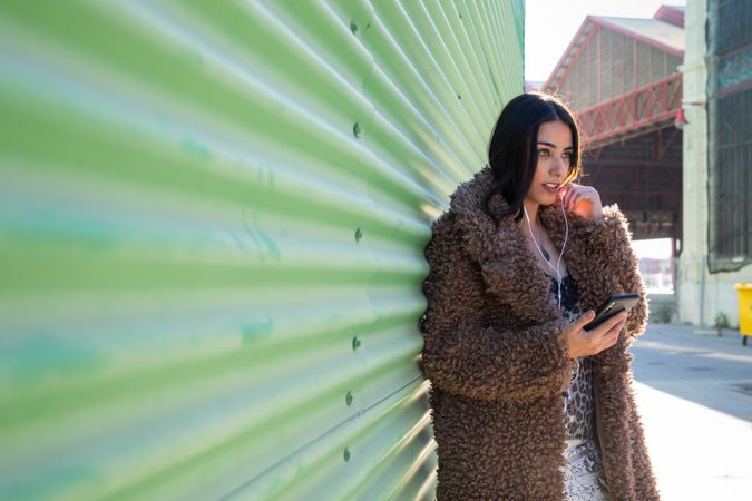 Trendy woman with smartphone near wall