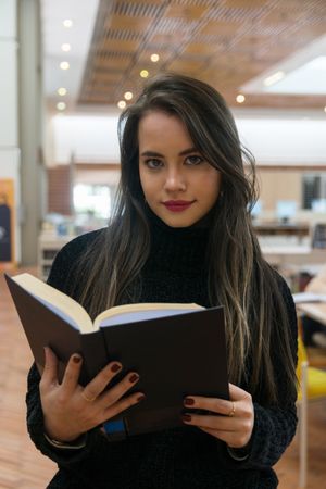 Woman standing along bookshelves and holding open book