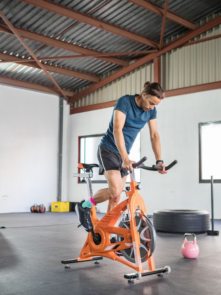 Sportsman exercising on stationary bicycle in light modern gym