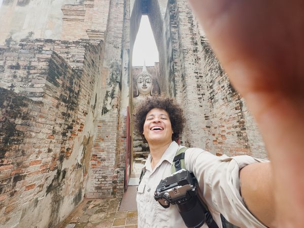 Joyful selfie capturing a traveler with smartphone and Buddha statue