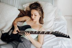 Young brunette woman playing guitar on bed