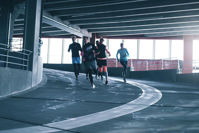 Group of people running down a sports track near bright window