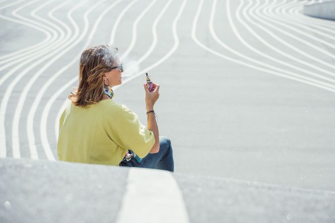 Modern relaxed woman vaping while sitting on marked road
