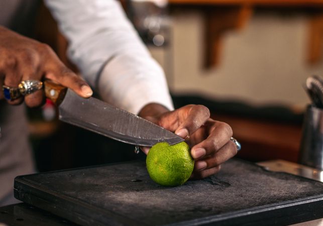 Close-up of an unrecognizable Black bartender in a hat cutting limes to prepare cocktails