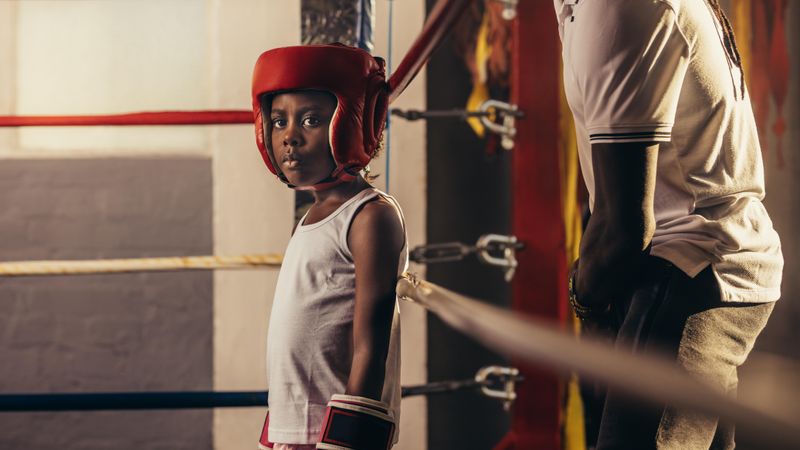 Girl wearing boxing gloves and headgear standing in a corner of a boxing ring