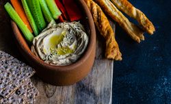 Creamy hummus dish served with chopped veggies on grey counter