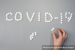Cropped image of a person arranging pills to write "Covid-19" 0LXKE0