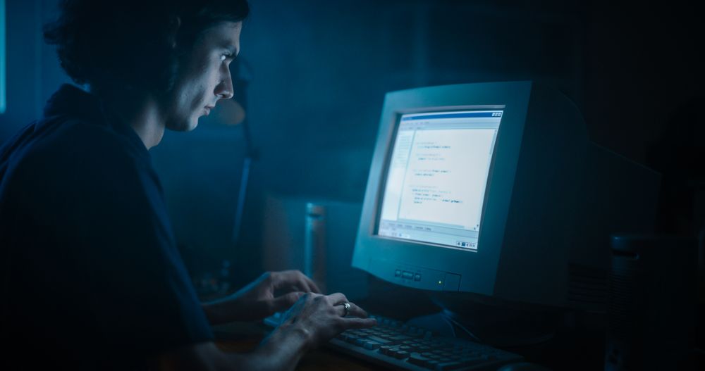 Male Web Designer Using Old Desktop Computer In Retro Garage Late At Night.