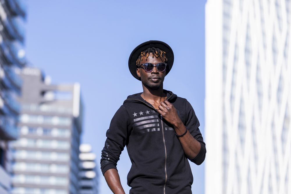 Black man wearing hat & sweater with sunglasses standing in the street