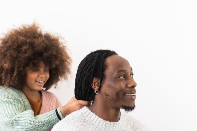 Amazed girl making hairdo on dreadlocks of father