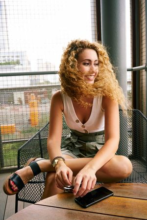Smiling woman sitting in designed metal chair with sunglasses in hand