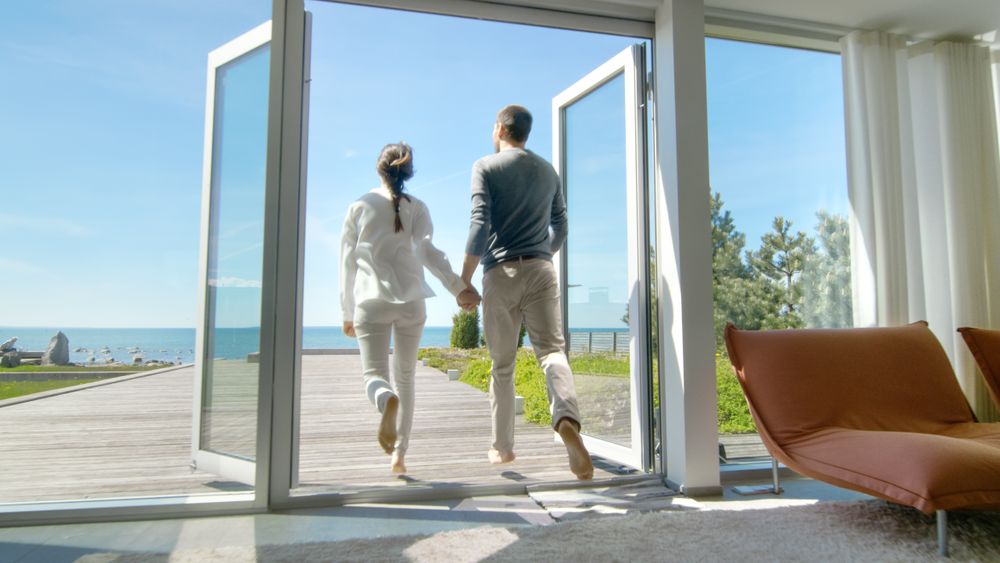 Happy Young Couple Holding Hands  Runs out of Their Home onto the Terrace with the Seaside View.