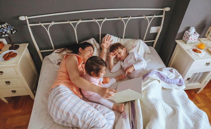 Top view of mother reading story to her daughter and son lying in the bed