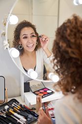 Cheerful young woman applying mascara on eyelashes while doing m
