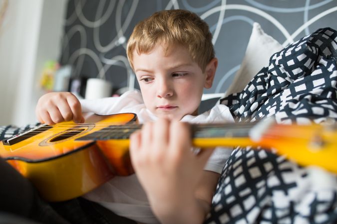Young blonde boy playing toy guitar