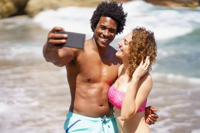 Man and woman taking selfie with waves in background