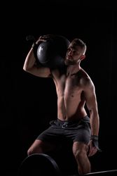 Muscular male athlete lifting fitness ball in dark gym