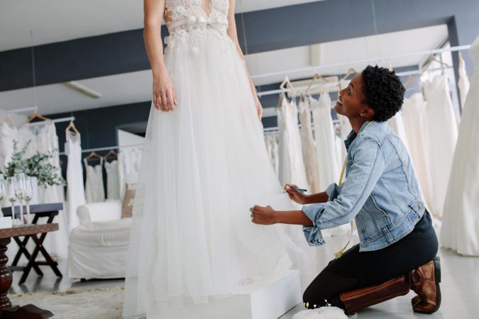 Woman making adjustment to bridal gown in wedding fashion store