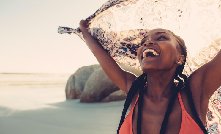 Beautiful woman laughing on the beach holding a large scarf