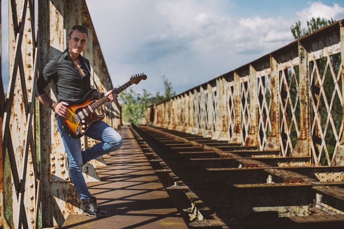 Man with guitar standing on bridge