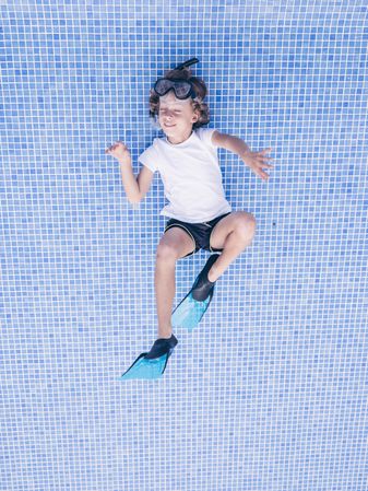 Excited preteen boy on bottom of empty pool imagining swimming