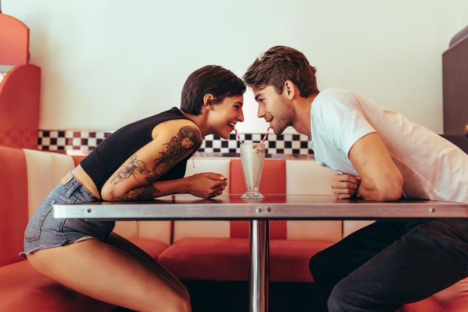 Couple in a restaurant looking at each other and sharing a milk shake with two straws
