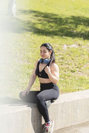 A young woman rests and relaxes with her eyes closed, sitting in the park, after exercising and playing sports