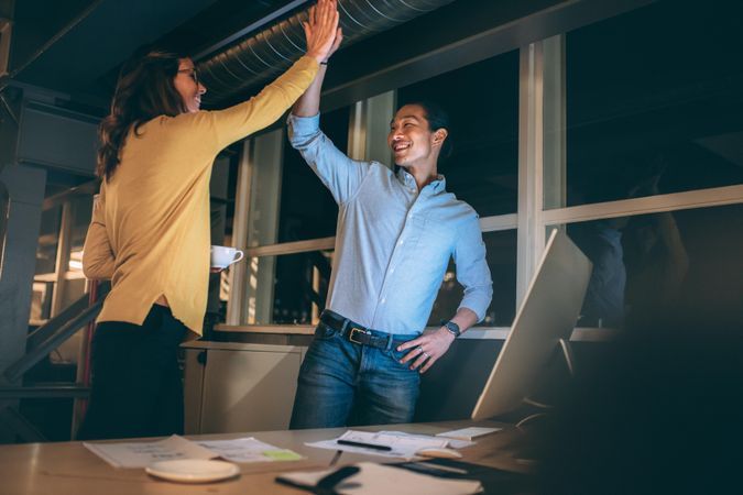 Businessman and woman giving high five standing in office working late in the night