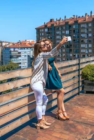 Two female friends taking a selfie in rooftop city on a summer day